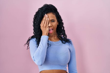 Photo for Middle age hispanic woman standing over pink background covering one eye with hand, confident smile on face and surprise emotion. - Royalty Free Image