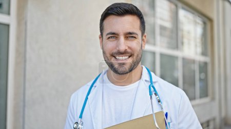 Photo for Young hispanic man doctor smiling confident holding medical report at hospital - Royalty Free Image