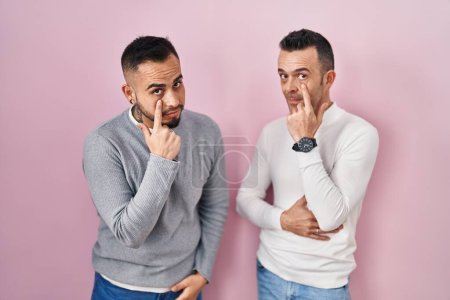 Photo for Homosexual couple standing over pink background pointing to the eye watching you gesture, suspicious expression - Royalty Free Image