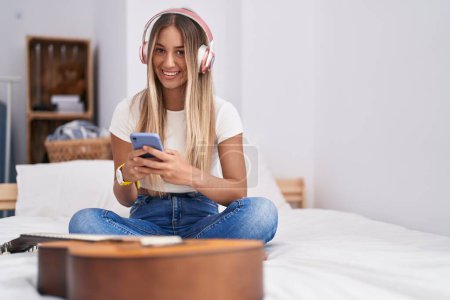 Photo for Young beautiful hispanic woman listening to music sitting on bed at bedroom - Royalty Free Image