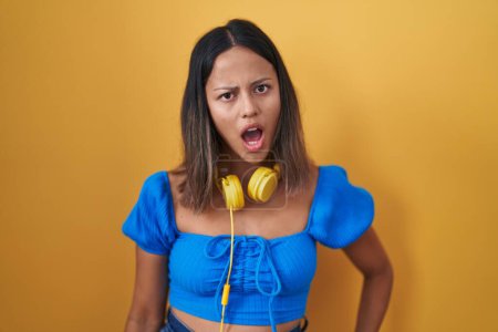 Foto de Mujer joven hispana de pie sobre fondo amarillo en la cara de choque, mirando escéptico y sarcástico, sorprendido con la boca abierta - Imagen libre de derechos