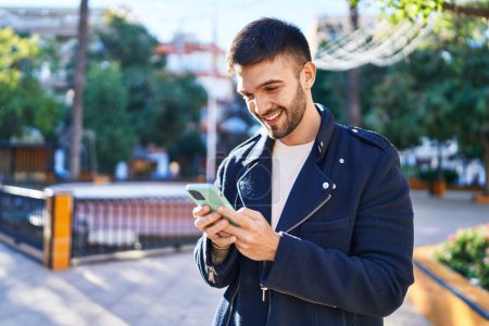 Téléchargez les photos : Jeune homme hispanique souriant confiant en utilisant un smartphone au parc - en image libre de droit