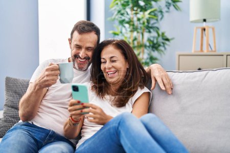 Foto de Mediana edad hombre y mujer pareja usando teléfono inteligente y beber café en casa - Imagen libre de derechos