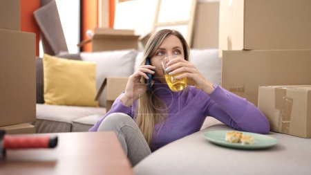 Téléchargez les photos : Jeune femme blonde parler sur smartphone infusion à boire à la nouvelle maison - en image libre de droit