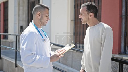 Téléchargez les photos : Deux hommes médecin et patient ayant une consultation médicale rédigeant un rapport à l'hôpital - en image libre de droit