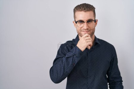 Photo for Young caucasian man standing over isolated background looking confident at the camera with smile with crossed arms and hand raised on chin. thinking positive. - Royalty Free Image