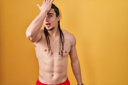 Photo for Hispanic man with long hair standing shirtless over yellow background surprised with hand on head for mistake, remember error. forgot, bad memory concept. - Royalty Free Image