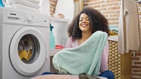 Foto de Mujer afroamericana lavando ropa oliendo toalla limpia en la lavandería - Imagen libre de derechos