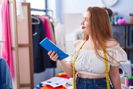 Téléchargez les photos : Young redhead woman tailor smiling confident using touchpad at clothing factory - en image libre de droit