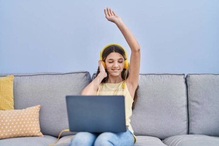 Téléchargez les photos : Adorable fille écouter de la musique assis sur le canapé à la maison - en image libre de droit