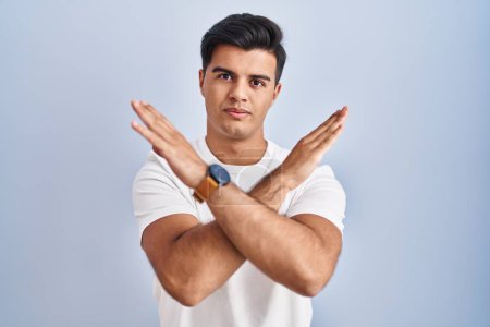 Téléchargez les photos : Hispanic man standing over blue background rejection expression crossing arms doing negative sign, angry face - en image libre de droit