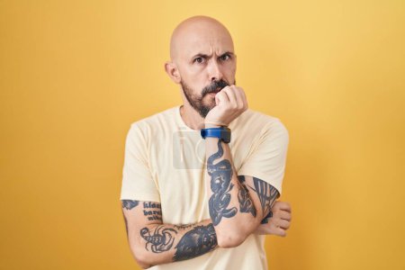 Photo for Hispanic man with tattoos standing over yellow background looking stressed and nervous with hands on mouth biting nails. anxiety problem. - Royalty Free Image