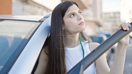Téléchargez les photos : Jeune belle femme hispanique ouvrant porte de voiture debout à la rue - en image libre de droit