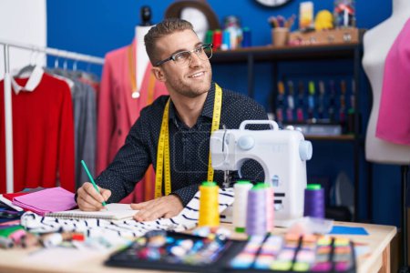 Téléchargez les photos : Jeune homme caucasien tailleur souriant dessin confiant sur ordinateur portable à l'usine de vêtements - en image libre de droit