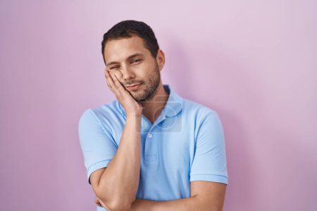 Foto de Hombre hispano de pie sobre fondo rosa pensando que parece cansado y aburrido con problemas de depresión con los brazos cruzados. - Imagen libre de derechos