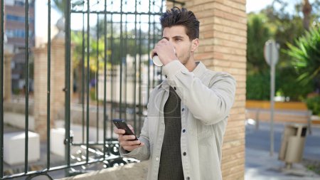 Photo for Young hispanic man talking on smartphone drinking coffee at street - Royalty Free Image