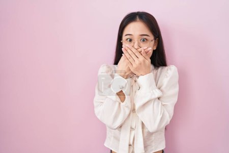 Téléchargez les photos : Jeune femme chinoise debout sur fond rose choqué couvrant la bouche avec les mains pour erreur. concept secret. - en image libre de droit