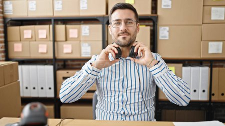 Photo for Young hispanic man ecommerce business worker smiling confident wearing headphones at office - Royalty Free Image
