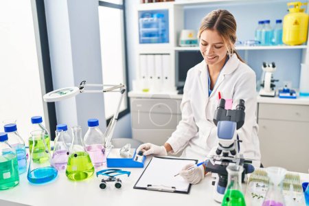 Photo for Young hispanic woman scientist weighing diamond writing report at laboratory - Royalty Free Image