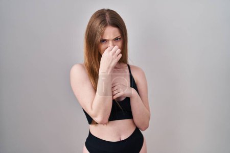 Foto de Mujer caucásica joven con lencería que huele algo apestoso y asqueroso, olor intolerable, conteniendo la respiración con los dedos en la nariz. mal olor - Imagen libre de derechos