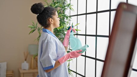 Téléchargez les photos : Femme afro-américaine nettoyer la fenêtre de nettoyage professionnel à la chambre d'hôtel - en image libre de droit