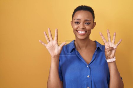 Foto de Mujer afroamericana de pie sobre fondo amarillo mostrando y señalando hacia arriba con los dedos número nueve mientras sonríe confiado y feliz. - Imagen libre de derechos