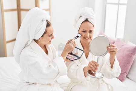 Foto de Two women mother and daughter wearing bathrobe applying skin makeup at bedroom - Imagen libre de derechos