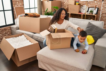 Photo for Mother and son unpacking cardboard box sitting on sofa at new home - Royalty Free Image