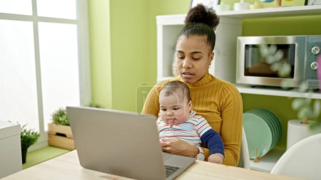 Photo for Mother and son sitting on table working online while care baby at dinning room - Royalty Free Image