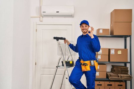 Photo for Young hispanic man working at renovation doing ok sign with fingers, smiling friendly gesturing excellent symbol - Royalty Free Image