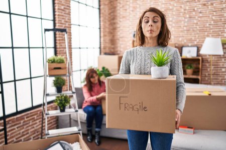 Photo for Mother and daughter moving to a new home holding cardboard box making fish face with mouth and squinting eyes, crazy and comical. - Royalty Free Image