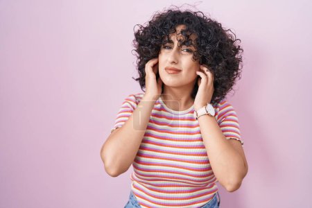 Photo for Young middle east woman standing over pink background covering ears with fingers with annoyed expression for the noise of loud music. deaf concept. - Royalty Free Image