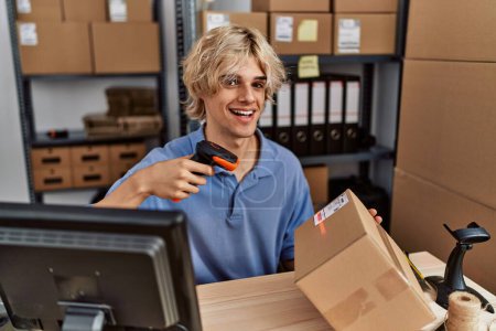 Téléchargez les photos : Jeune homme blond commerce électronique travailleur d'affaires numérisation paquet au bureau - en image libre de droit