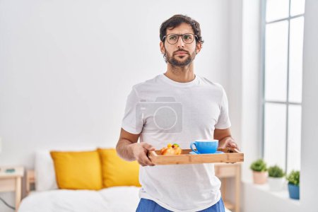 Foto de Hombre latino guapo desayunando en la cama sonriendo mirando a un lado y mirando a otro pensando. - Imagen libre de derechos