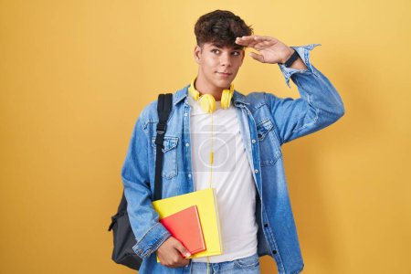 Photo for Hispanic teenager wearing student backpack and holding books very happy and smiling looking far away with hand over head. searching concept. - Royalty Free Image