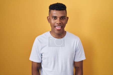 Photo for Young hispanic man standing over yellow background sticking tongue out happy with funny expression. emotion concept. - Royalty Free Image