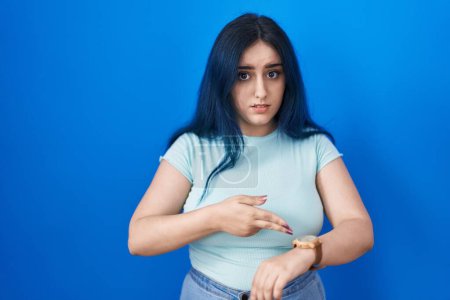 Photo for Young modern girl with blue hair standing over blue background in hurry pointing to watch time, impatience, upset and angry for deadline delay - Royalty Free Image