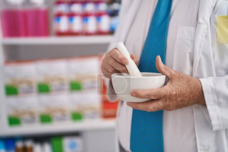 Photo for Middle age grey-haired man pharmacist make mixture at pharmacy - Royalty Free Image