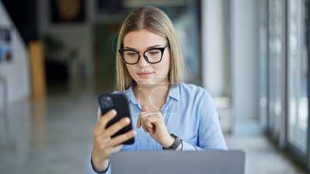 Téléchargez les photos : Jeune femme blonde travailleuse d'entreprise utilisant un smartphone travaillant au bureau - en image libre de droit