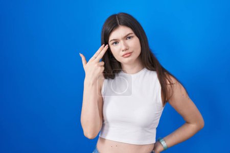 Téléchargez les photos : Young caucasian woman standing over blue background shooting and killing oneself pointing hand and fingers to head like gun, suicide gesture. - en image libre de droit