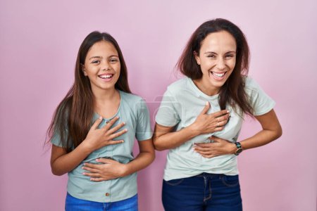 Photo for Young mother and daughter standing over pink background smiling and laughing hard out loud because funny crazy joke with hands on body. - Royalty Free Image