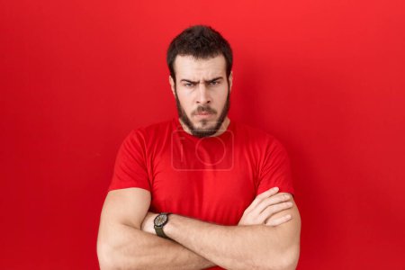 Téléchargez les photos : Jeune homme hispanique portant un t-shirt rouge décontracté, sceptique et nerveux, désapprouvant l'expression sur le visage avec les bras croisés. personne négative. - en image libre de droit