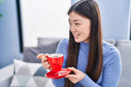 Téléchargez les photos : Femme chinoise buvant du café assis sur le canapé à la maison - en image libre de droit