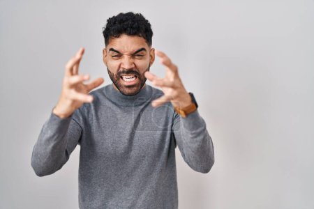 Photo for Hispanic man with beard standing over white background shouting frustrated with rage, hands trying to strangle, yelling mad - Royalty Free Image