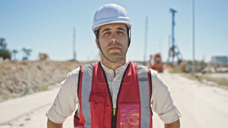 Téléchargez les photos : Jeune homme hispanique constructeur debout avec une expression détendue à la rue - en image libre de droit