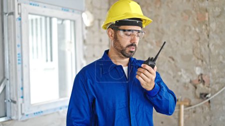 Téléchargez les photos : Jeune homme hispanique travailleur parlant sur talkie-walkie sur le chantier de construction - en image libre de droit
