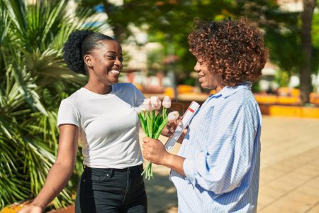 Téléchargez les photos : Femmes afro-américaines mère et fille surprise avec bouquet de fleurs au parc - en image libre de droit
