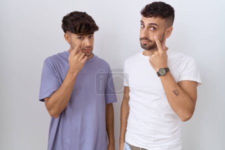 Téléchargez les photos : Couple gay homosexuel debout sur fond blanc pointant vers l'oeil vous regarder geste, expression suspecte - en image libre de droit