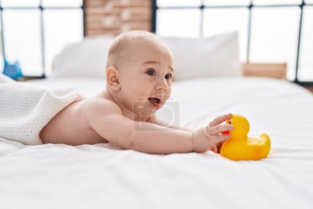 Photo for Adorable caucasian baby lying on bed holding duck toy at bedroom - Royalty Free Image