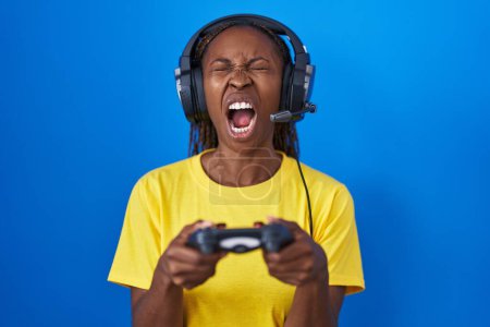 Photo for African american woman playing video games angry and mad screaming frustrated and furious, shouting with anger looking up. - Royalty Free Image